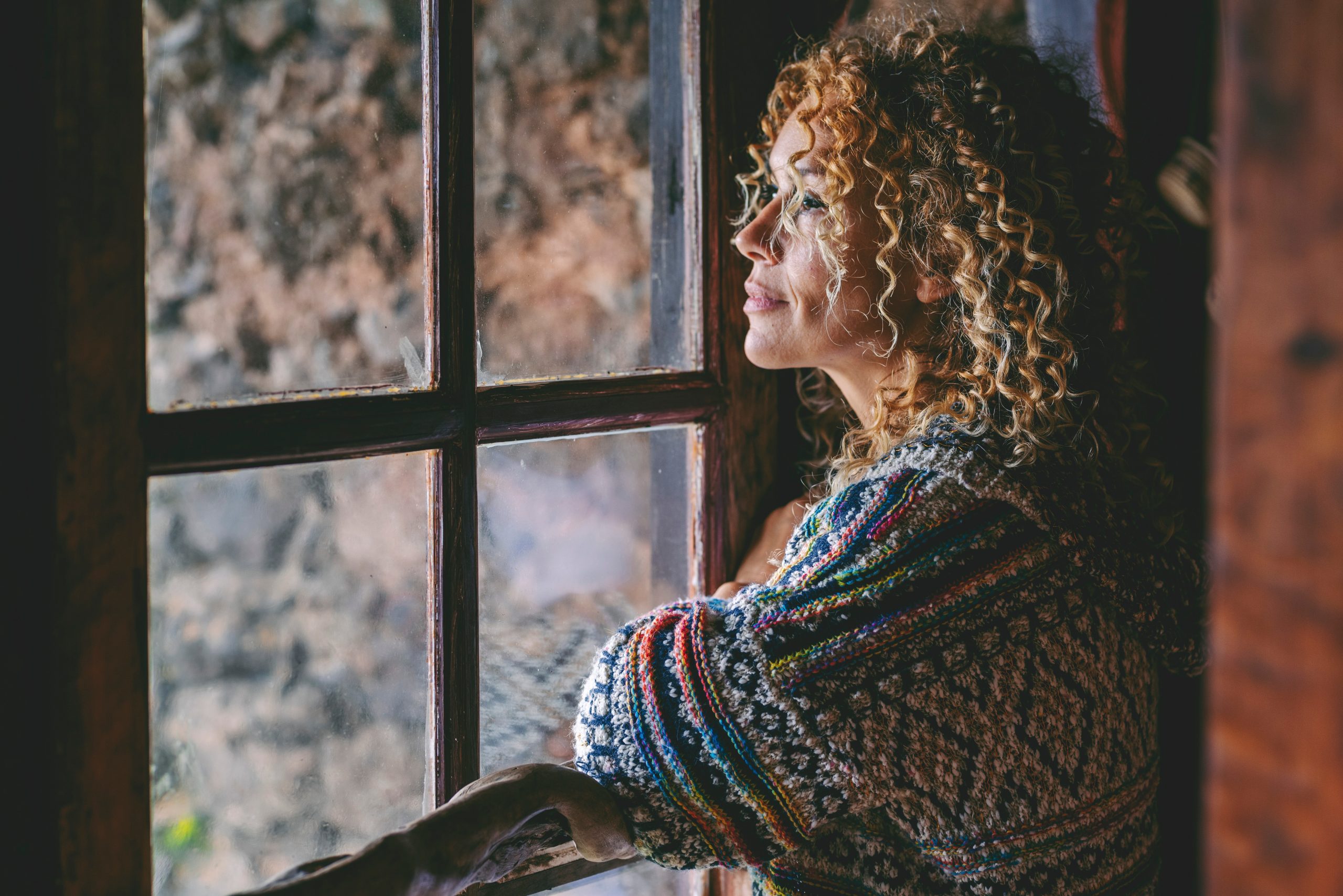 One alone woman standing at home near the window looking outside and thinking. Single female people lifestyle. Waiting friends and thoughts. Young lady indoor leisure. Side portrait of middle age at home abortion